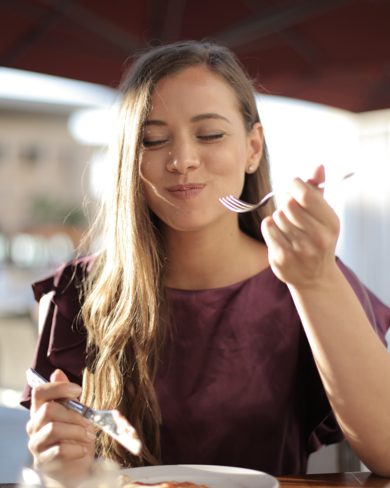 A woman with smiles club clear aligners eating outside.